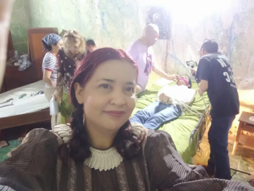 Una de las actrices, ya vestida para su papel, se toma una foto mientras detrás preparan la escena de la cama y se graba con un teléfono.