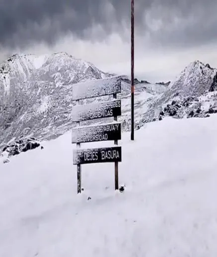 Cartelera de normas del parque, medio enterrada en la nieve, con la cordillera nevada detrás: se alcanza a leer «no dejes basura» y las advertencias sobre las especies endémicas y el agua.
