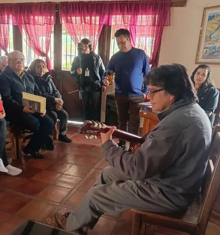 Un guitarrista toca para los presentes durante el acto, mientras el homenajeado escucha con sus libros en el regazo.