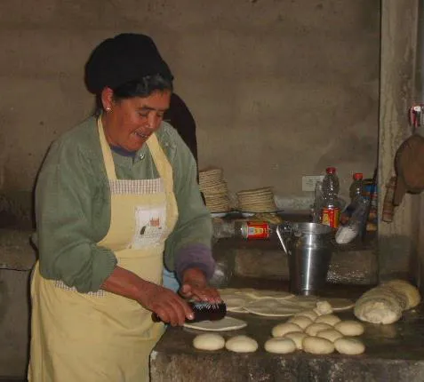 Una mujer con delantal aplana las bolas de masa sobre el mesón; a un lado, las arepas ya formadas y las pilas de las que salieron del budare.