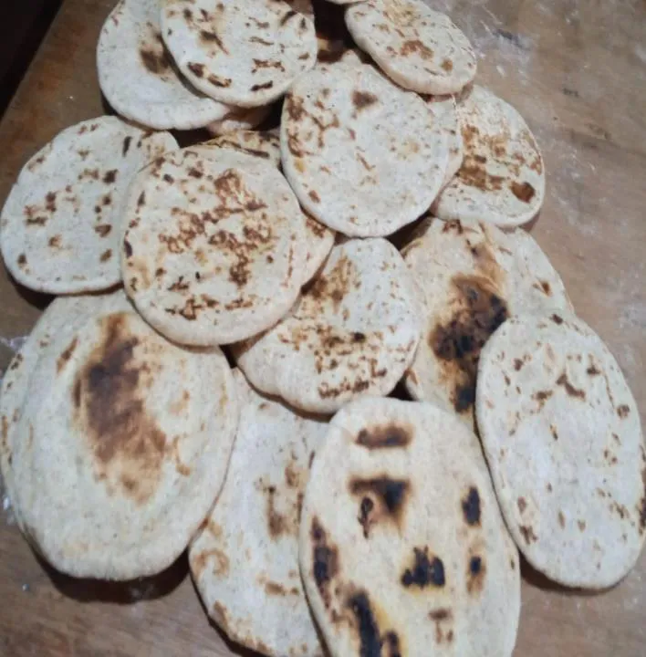 Las arepas de trigo asadas, amontonadas sobre la mesa de madera con las manchas desiguales que deja el budare.