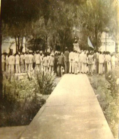 Fotografía antigua en sepia: una fila larga de hombres formados a lo largo de un paseo arbolado.