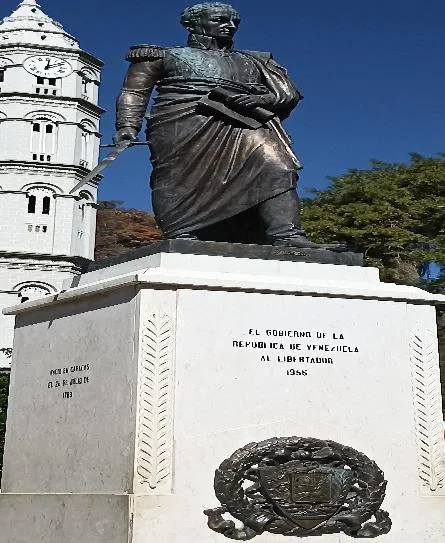 La estatua del Libertador de frente, con la placa del pedestal y la fachada blanca de la basílica detrás.