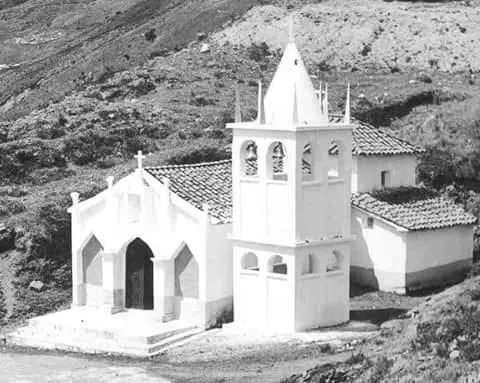 La capilla blanca de Cruz Chiquita, de una sola nave y espadaña calada, recortada en blanco y negro contra la ladera del páramo.