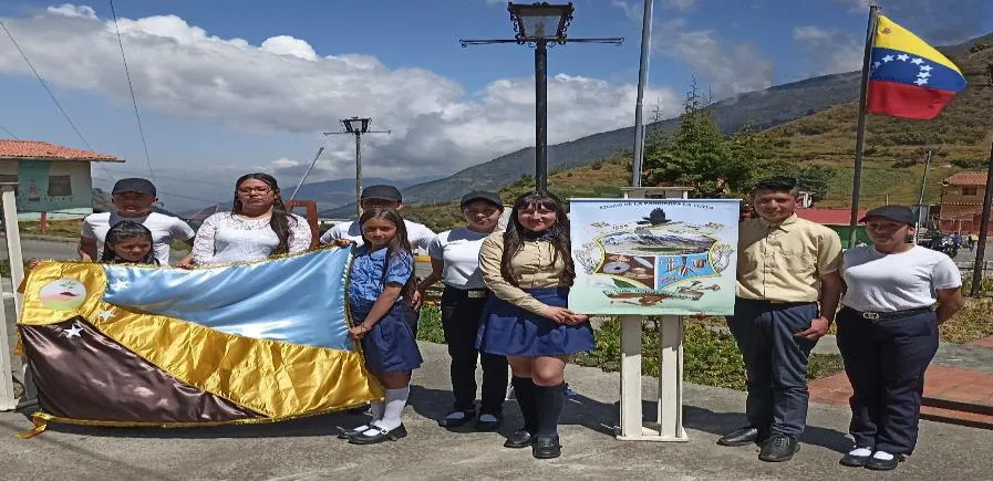 Escolares con una bandera amarilla y azul en el acto de oficialización de los símbolos parroquiales, en la plaza de La Venta.