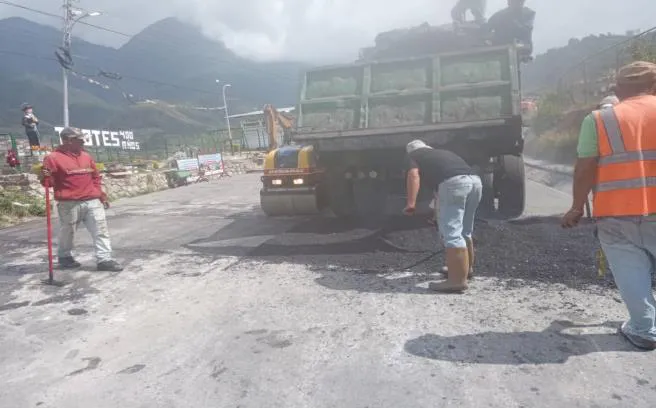 El camión descargando el asfalto caliente mientras los obreros lo reparten con rastrillos.