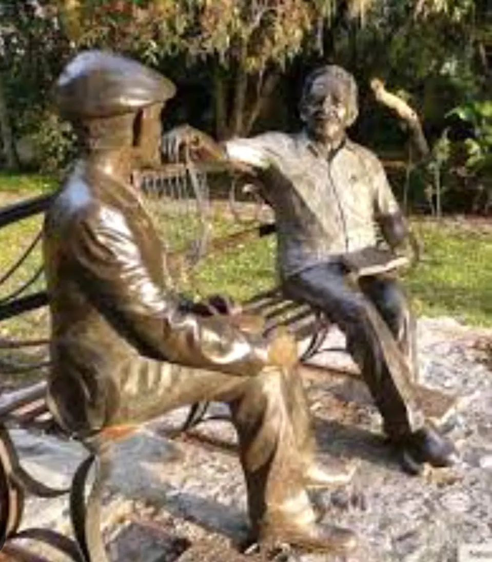 Dos figuras de bronce conversan sentadas en un banco de parque.