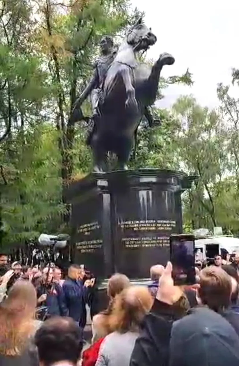 El público fotografía con sus teléfonos la estatua ecuestre de Bolívar recién descubierta, entre árboles altos.