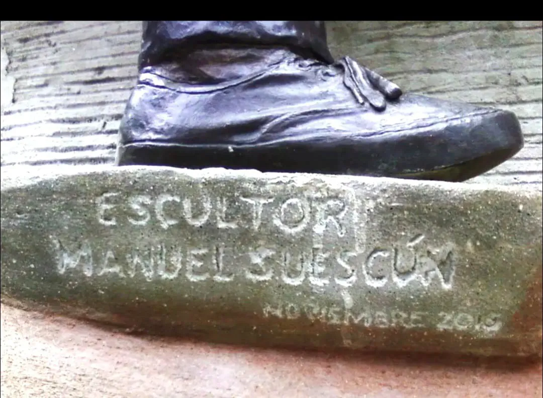 La firma grabada en la base de una escultura, junto al zapato de la figura: «Escultor Manuel Suescún», con la fecha de noviembre.