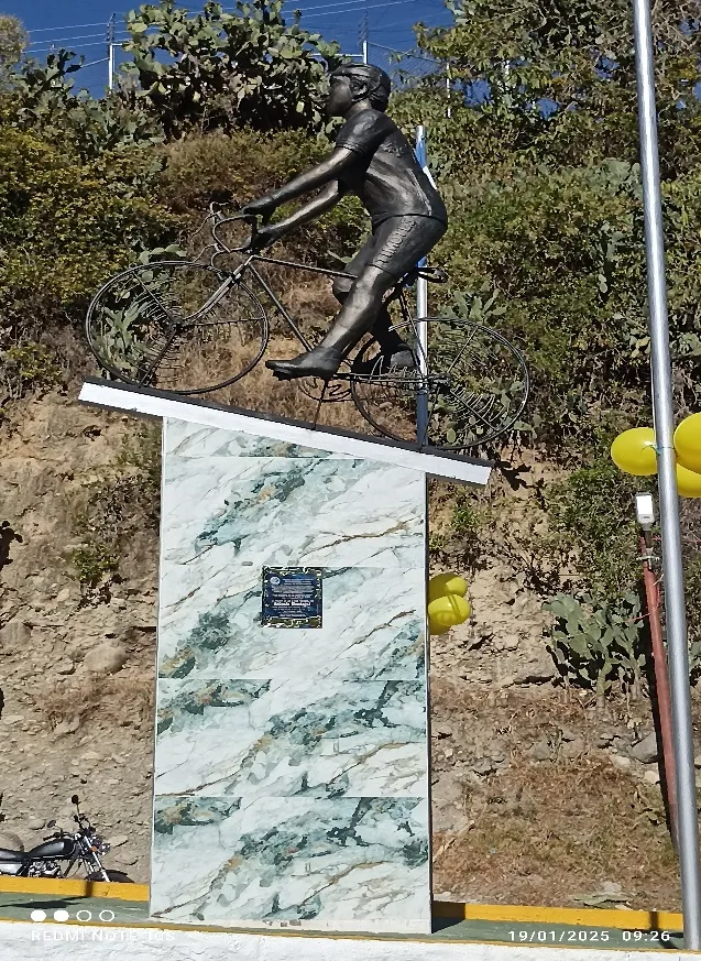 El pedestal forrado de cerámica veteada, con la placa al centro y la escultura encima, adornado con globos amarillos.