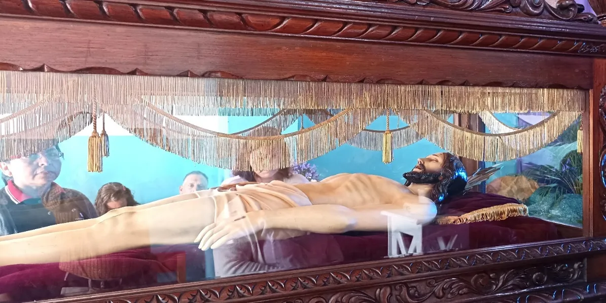 La imagen del Cristo yacente en su urna de cristal, con flecos dorados, y los fieles detrás.