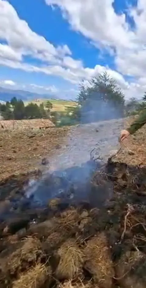 Suelo paramero humeando tras la quema, con viviendas y sembradíos al fondo.
