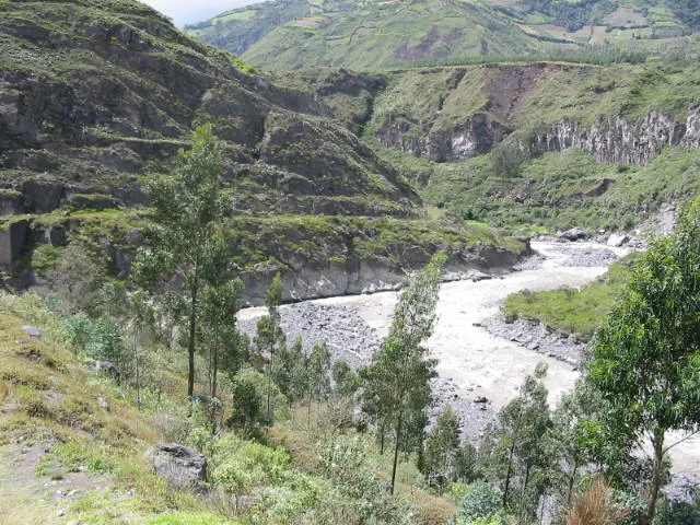 Un río de aguas blancas que corre entre montañas verdes y árboles.