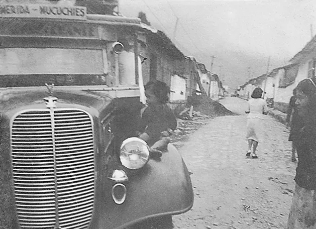 Fotografía antigua de la calle de entrada al pueblo, con un camión de los años treinta en primer plano.
