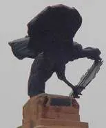 Escultura oscura sobre un pedestal de ladrillo, fotografiada contra el cielo.