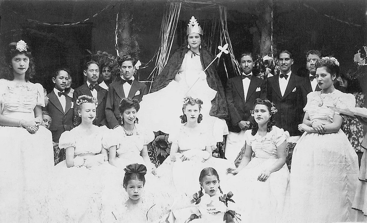 Fotografía antigua de un carnaval: una reina con corona y su corte de damas y caballeros.
