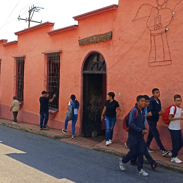 La Casa de la Cultura «Don Jesús María Espinoza B.», pintada de salmón, con el ángel de alambre en la fachada y los estudiantes pasando por la acera.