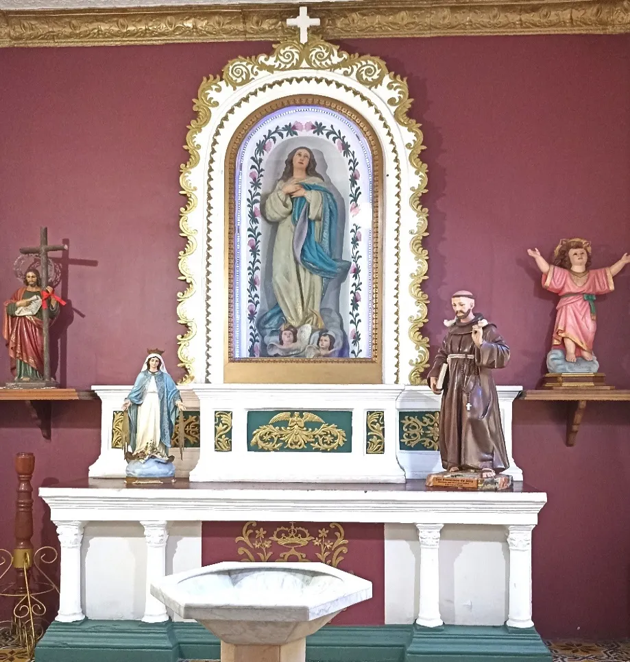 Altar lateral con el cuadro de la Inmaculada bajo su marco dorado, las imágenes de bulto a los lados y la pila bautismal de mármol delante.