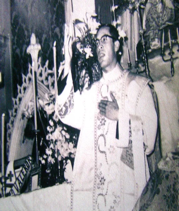 Un sacerdote joven eleva la hostia ante el altar florido, en una fotografía antigua; en el paño del altar se lee «Valero».