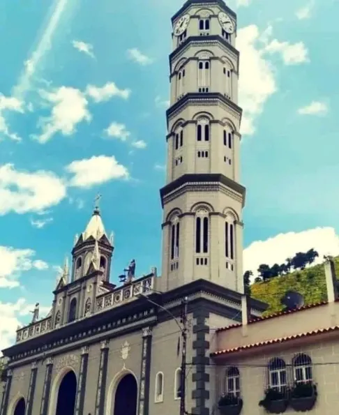 La Basílica y su torre recortadas contra un cielo de nubes altas, con el cerro verde al costado.