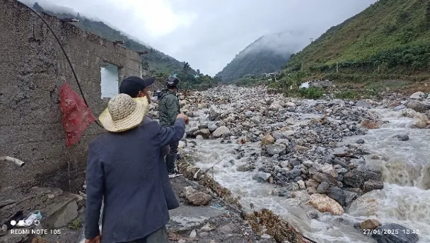 Vecinos asomados al cauce después de la crecida, junto a una casa descarnada por el agua y el reguero de piedras.