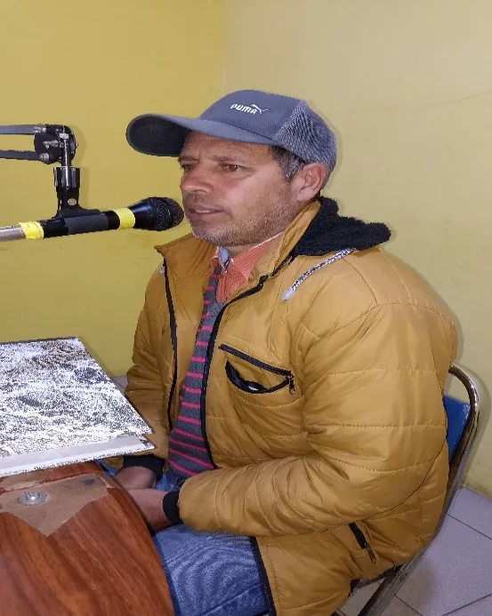 Un hombre de gorra habla ante el micrófono en la cabina de la emisora, con sus papeles sobre el atril.