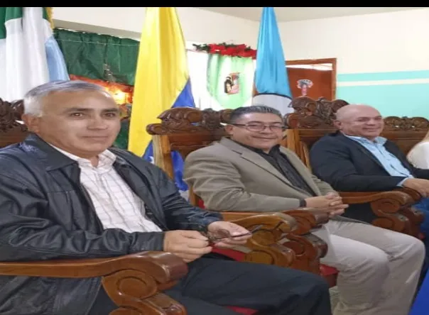 Tres hombres sentados en los sillones de madera labrada del salón del Concejo, entre las banderas.