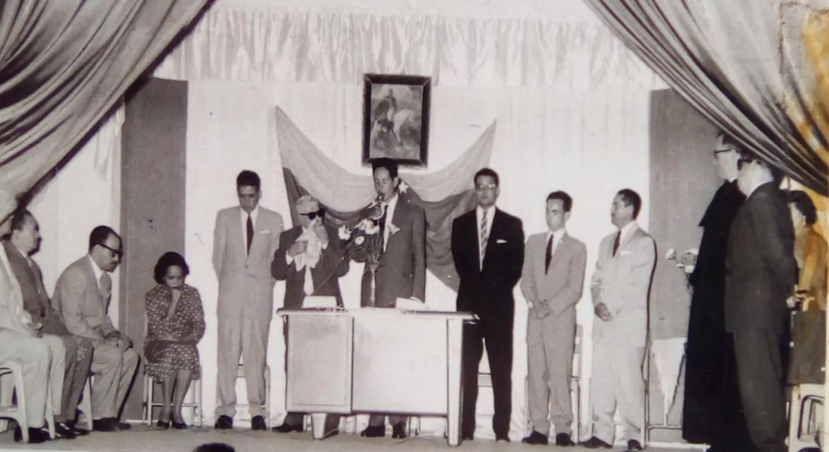 Acto público con el Maestro, de lentes oscuros, en el estrado.