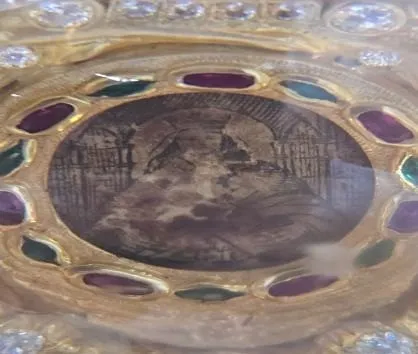 Relicario dorado con piedras de colores alrededor de una imagen antigua.