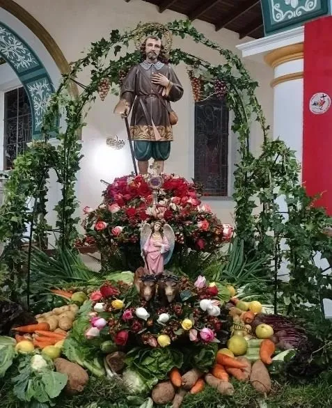 La imagen de San Isidro Labrador bajo un arco de hojas, entre flores, frutas y hortalizas.