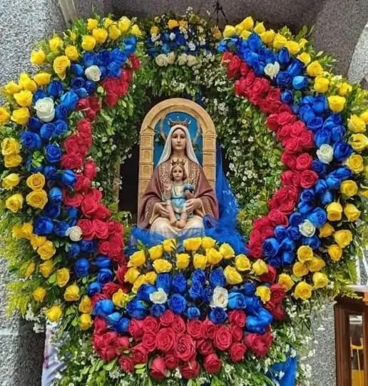 Imagen de la Virgen con el Niño en un nicho, rodeada por una corona de rosas amarillas, azules y rojas.