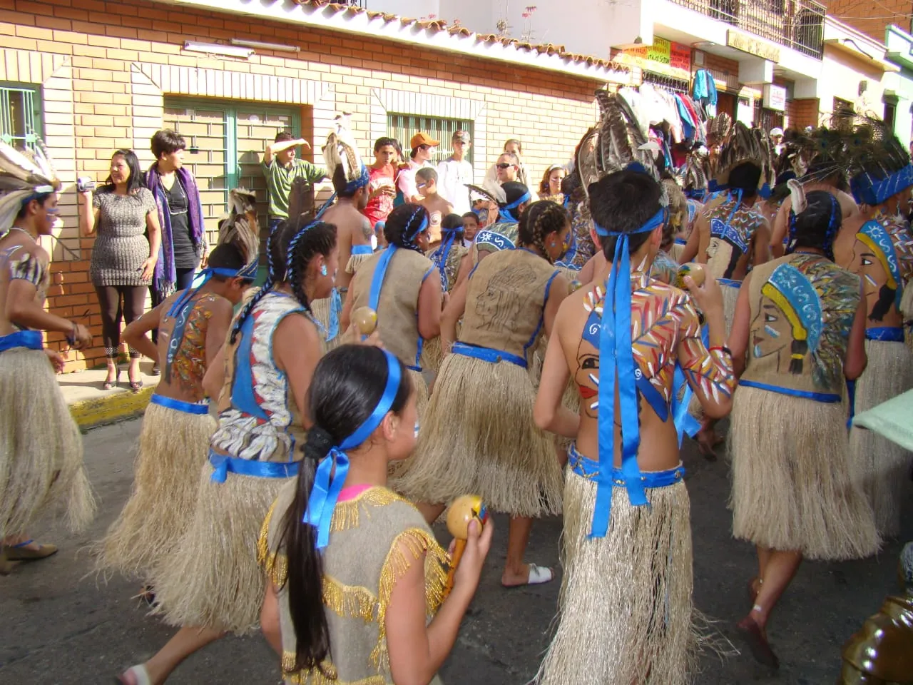 La comparsa de indios entera bajando por la calle, con las espaldas pintadas de rostros y plumas.