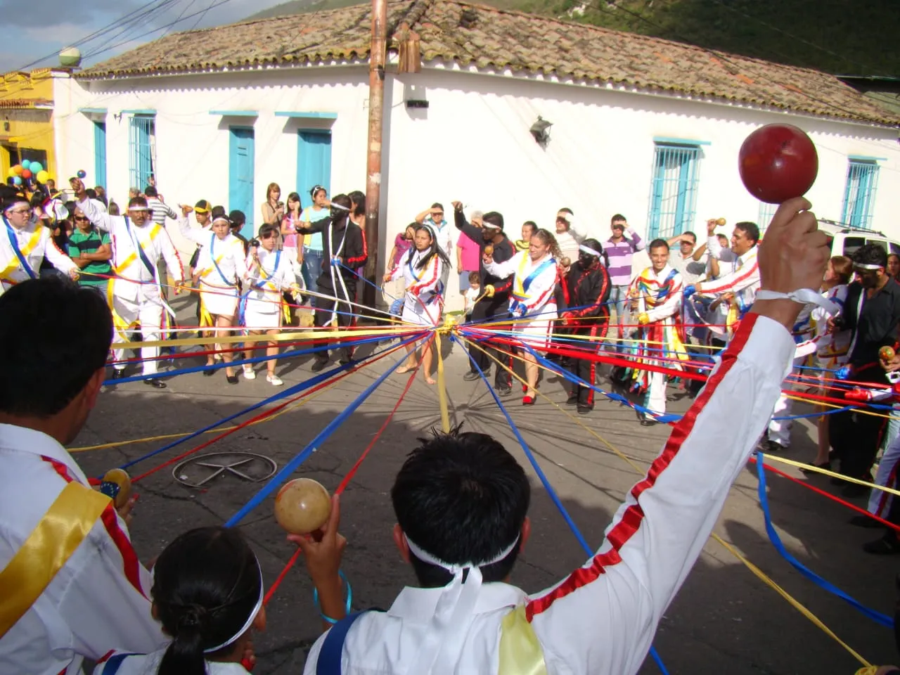 Baile de las cintas: los danzantes de blanco tejen el palo desde la rueda, con las maracas en alto.