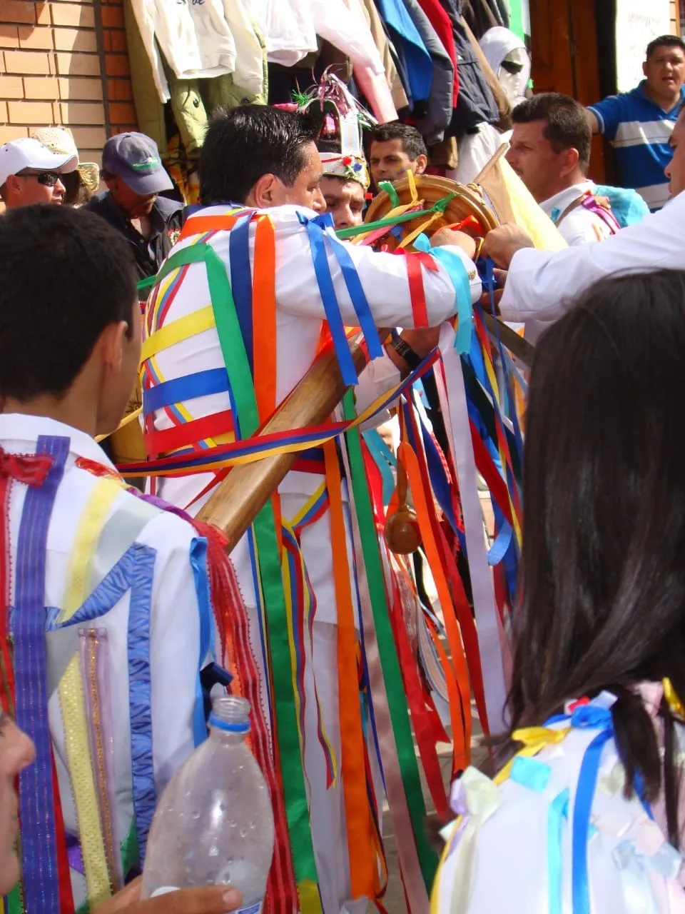 Uno de los danzantes carga el palo de cintas al hombro, con todas las cintas de colores colgando, mientras el grupo avanza por la calle.