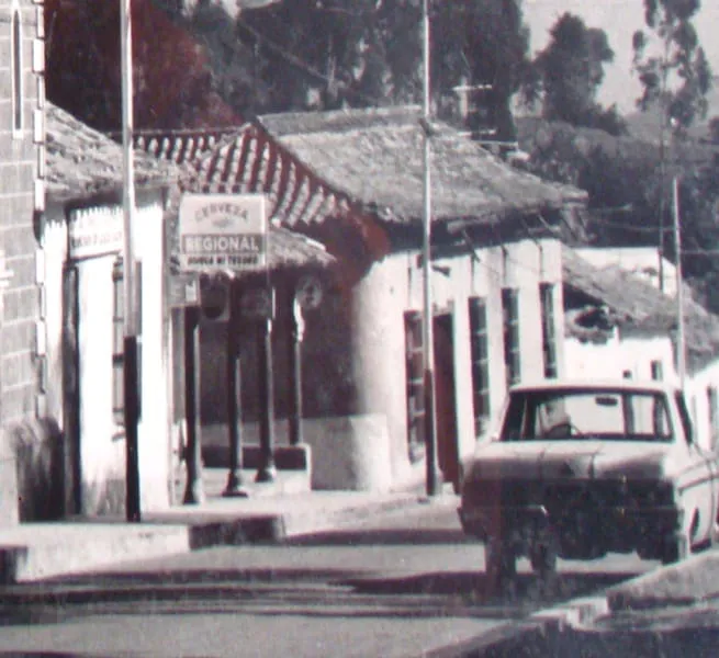 Calle de Timotes en blanco y negro, con un aviso de Cerveza Regional bajo el alero, los postes de madera y una camioneta de los años sesenta.