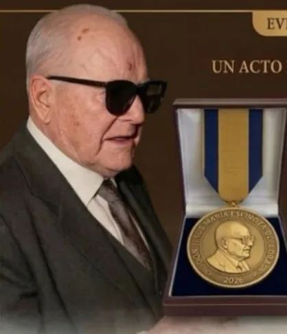 Un señor mayor sostiene el estuche con la medalla «Jesús María Espinoza», fechada en 2026, con el retrato en relieve y la cinta azul y amarilla.