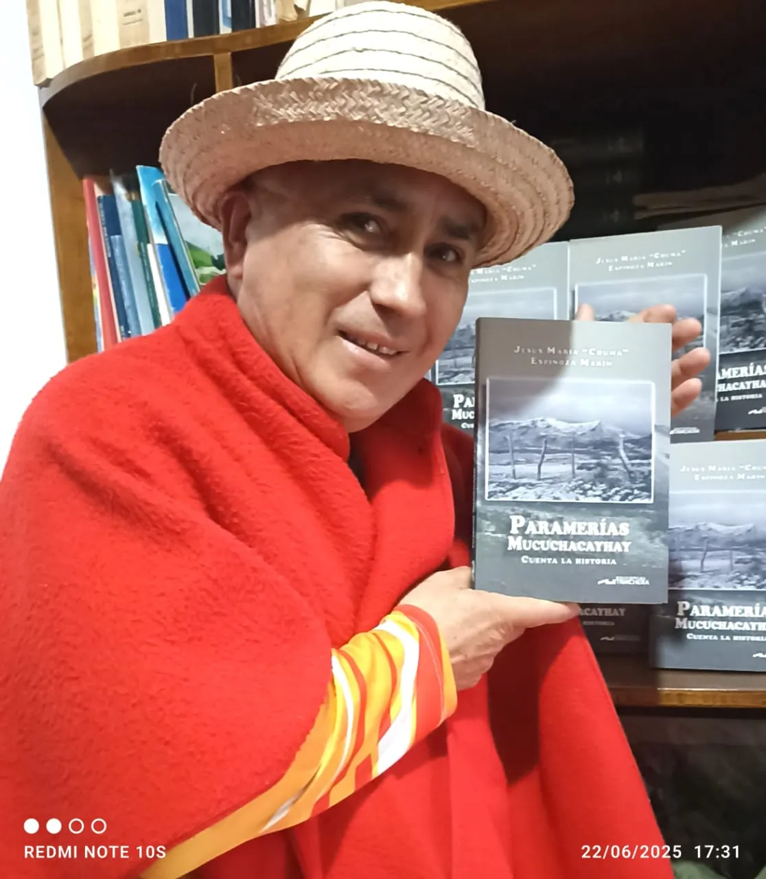 El cronista, con ruana roja y sombrero de cogollo, muestra «Paramerías Mucuchacayhay cuenta la historia»; detrás, el estante lleno de ejemplares.