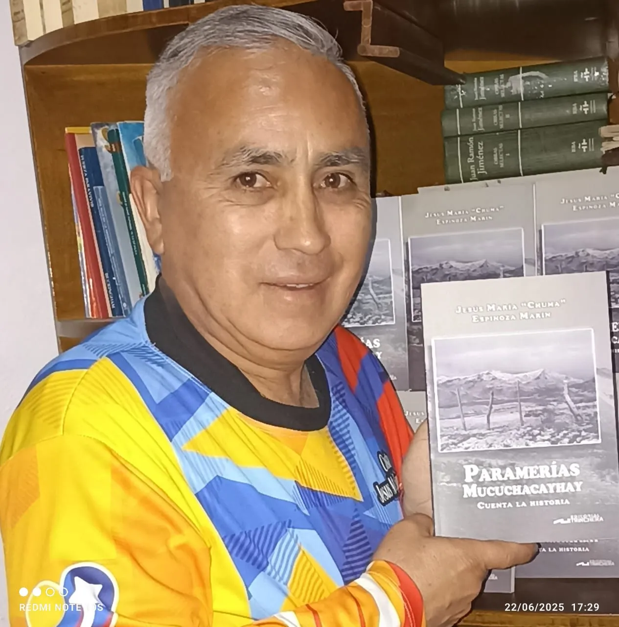 El cronista muestra «Paramerías Mucuchacayhay cuenta la historia» ante su biblioteca, con los ejemplares apilados detrás.